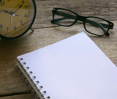 photo of a clock, notepad and eye glasses 